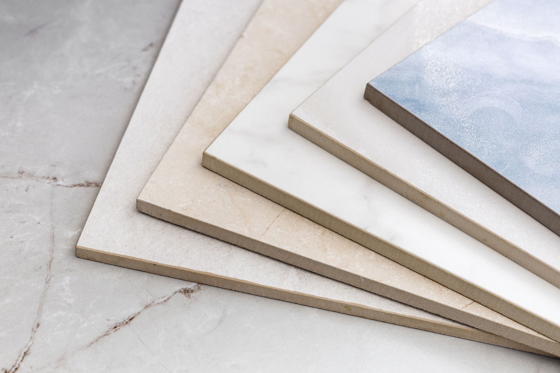 Various rectangular ceramic tiles in neutral colors, stacked and displayed on a marble surface.