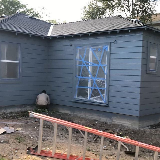 A man is sitting on the side of a house with a ladder in front of it