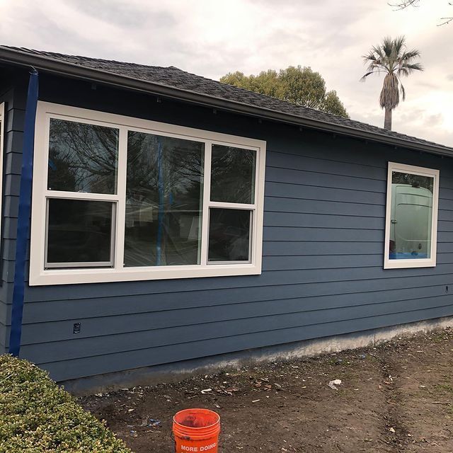 A blue house with white windows and a bucket in front of it.