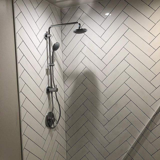 A shower with a herringbone pattern on the wall and a shower head.