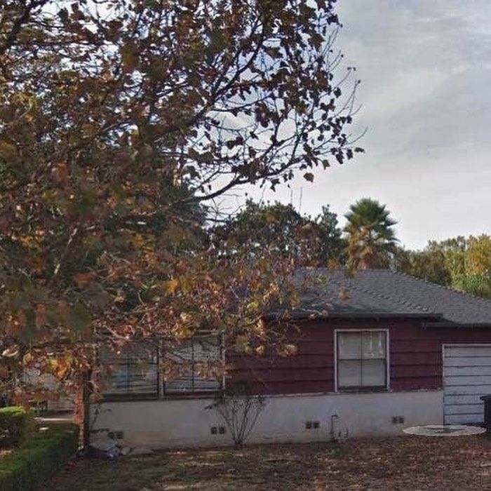 A red house with a garage and a tree in front of it