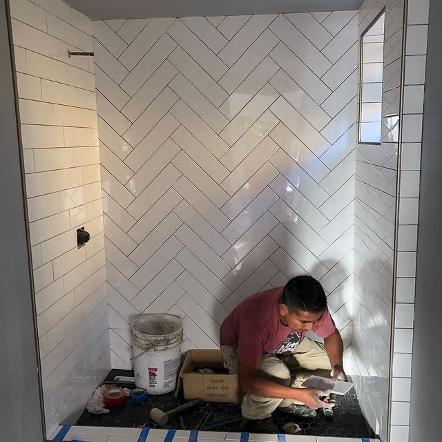 A man is kneeling down in a bathroom with white tiles.