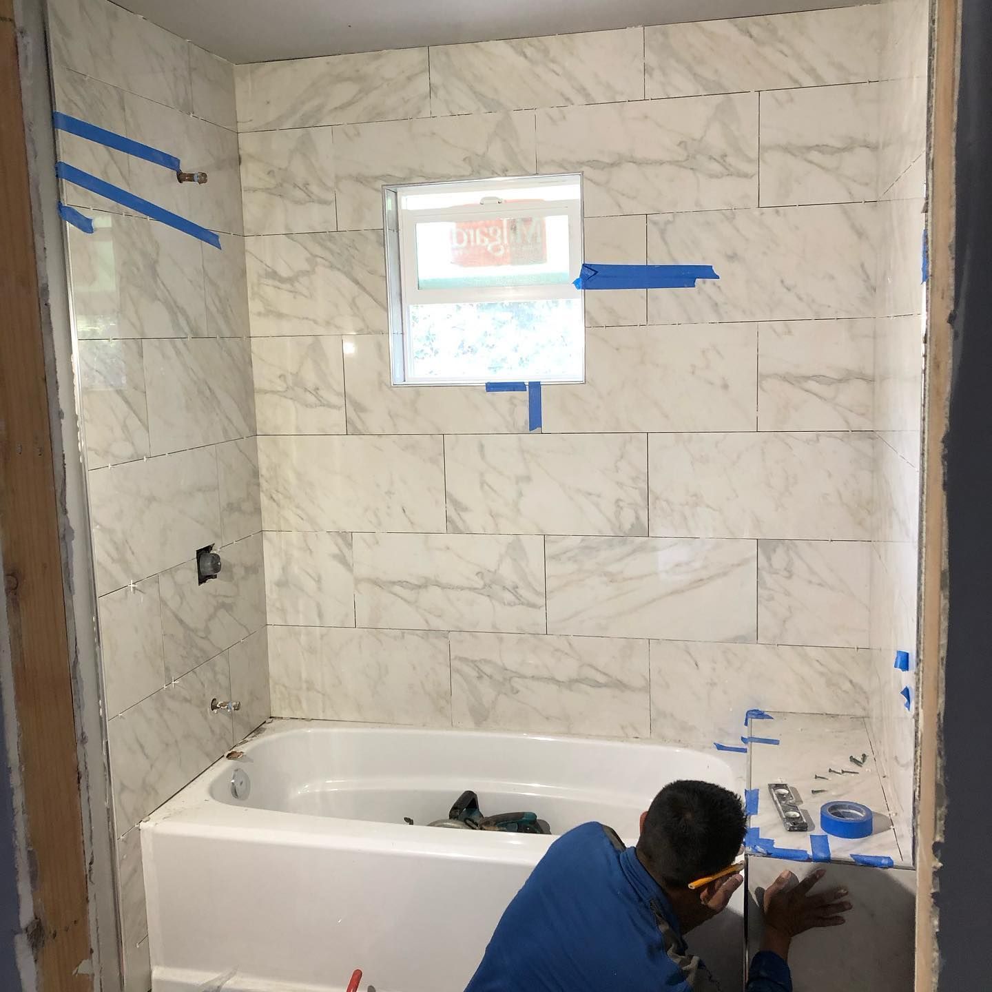 A man is kneeling in front of a bathtub in a bathroom.