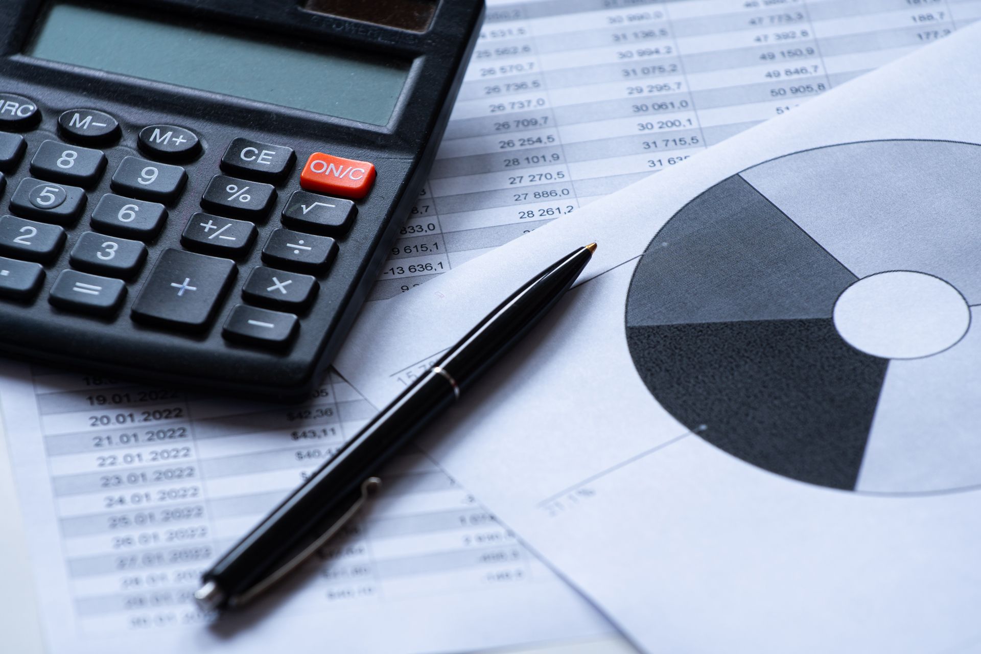 Calculator, pen, and pie chart on a financial document, showing data analysis