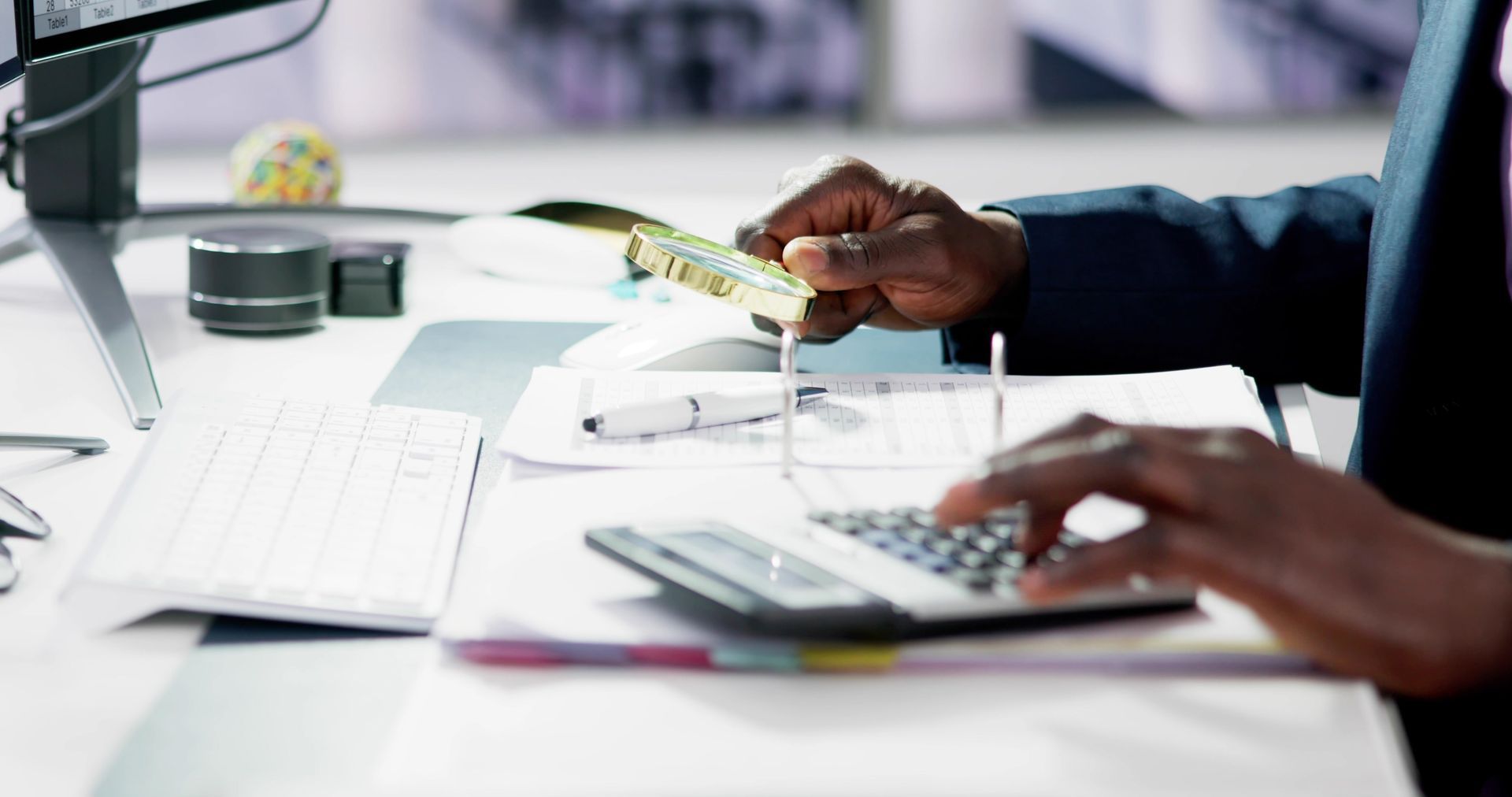 Person in suit using a calculator and holding receipts at a desk.