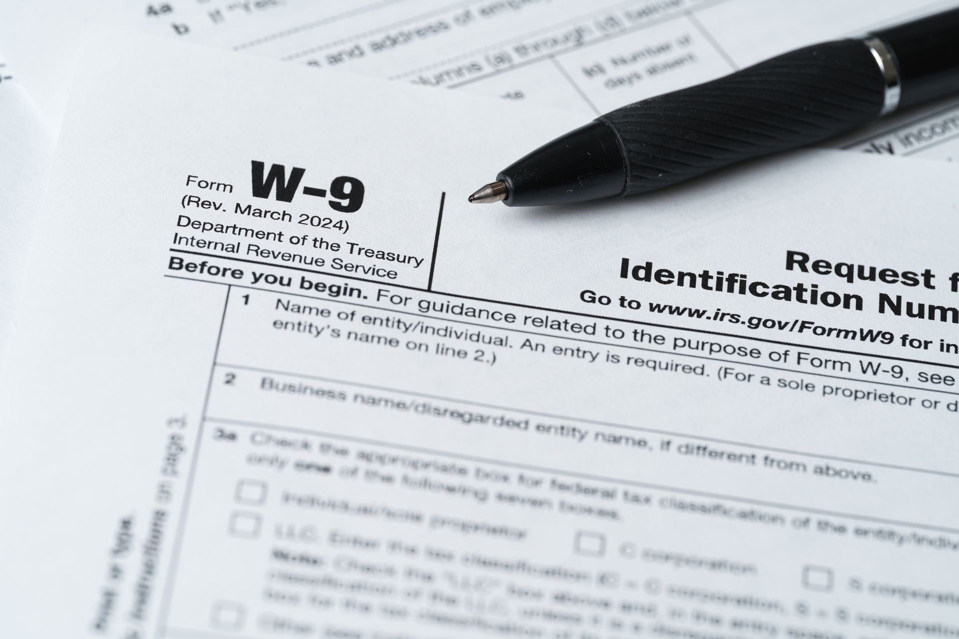 A black pen rests on a partially filled IRS W-9 form; white paper