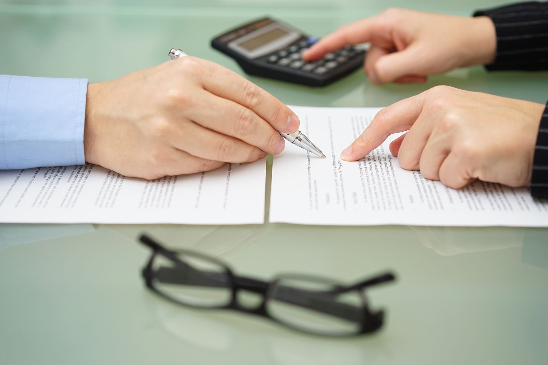Two people signing a document with a calculator nearby and glasses on a table