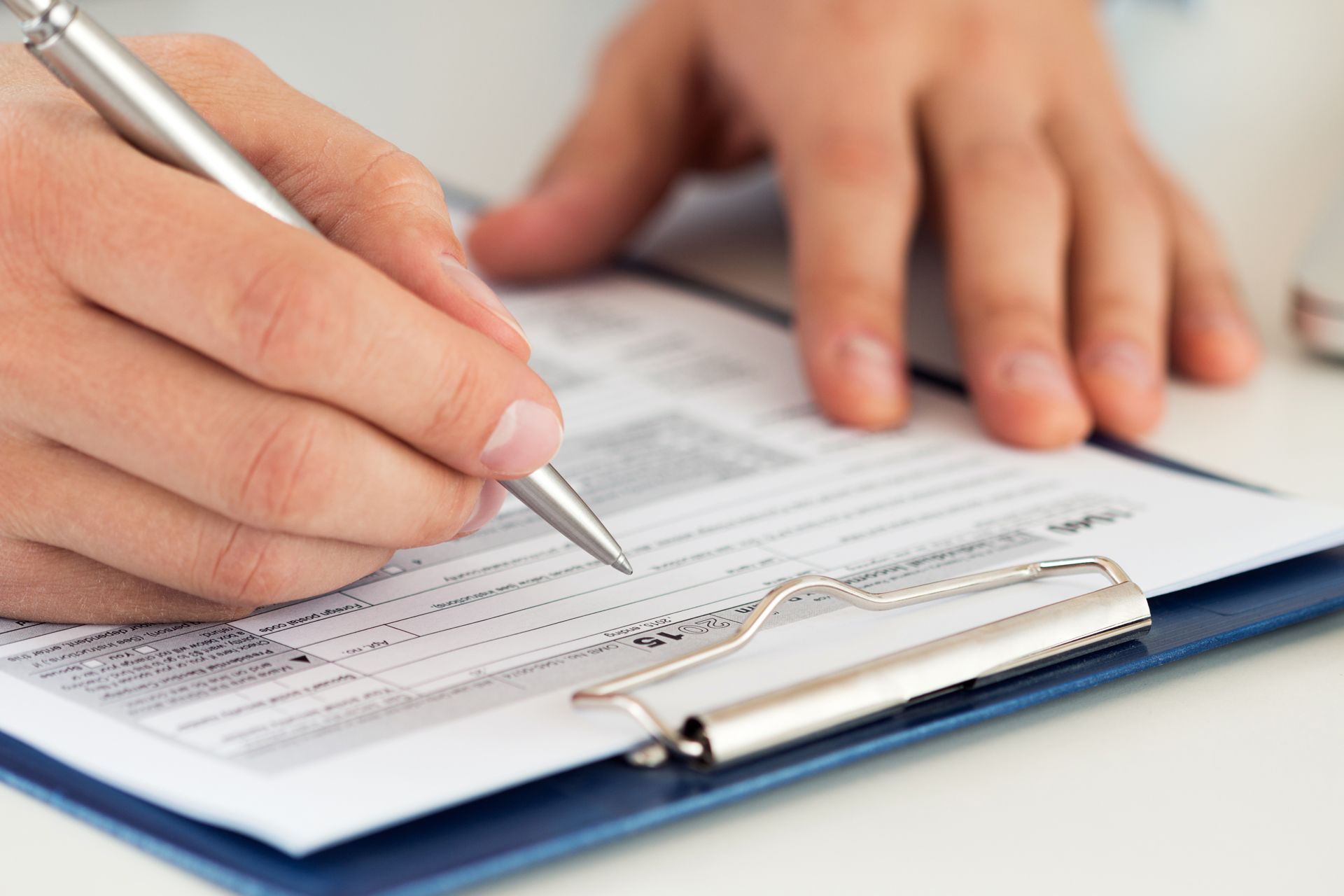 Person writing on a form with a pen, held on a clipboard