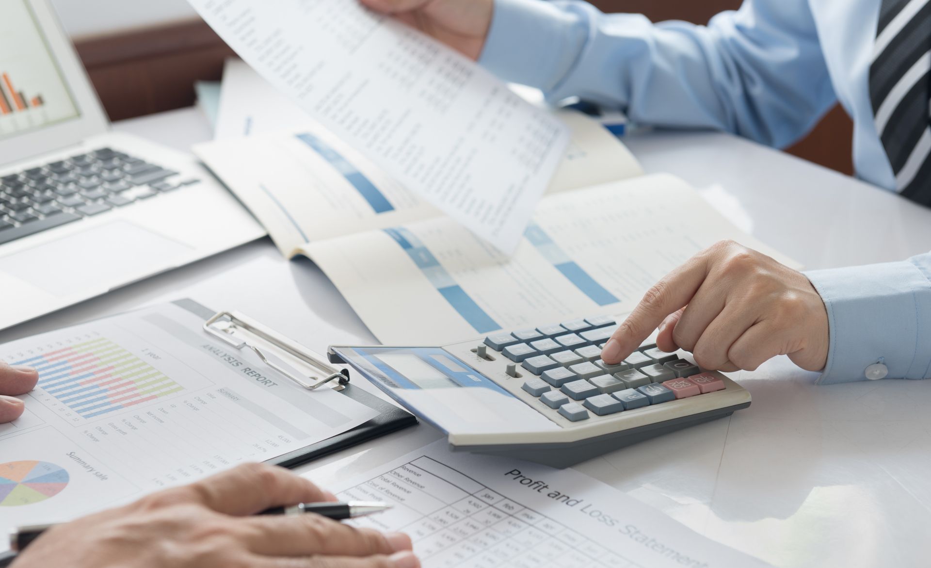 Two people reviewing financial documents with a calculator and laptop in an office setting