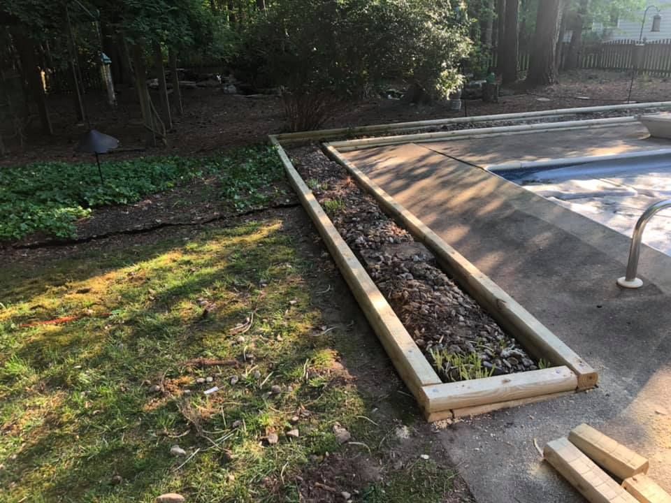 A wooden planter is sitting next to a swimming pool.