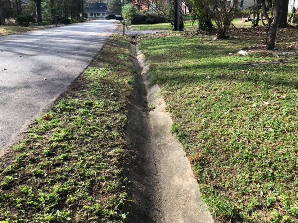 A drain on the side of a road next to a grassy area.