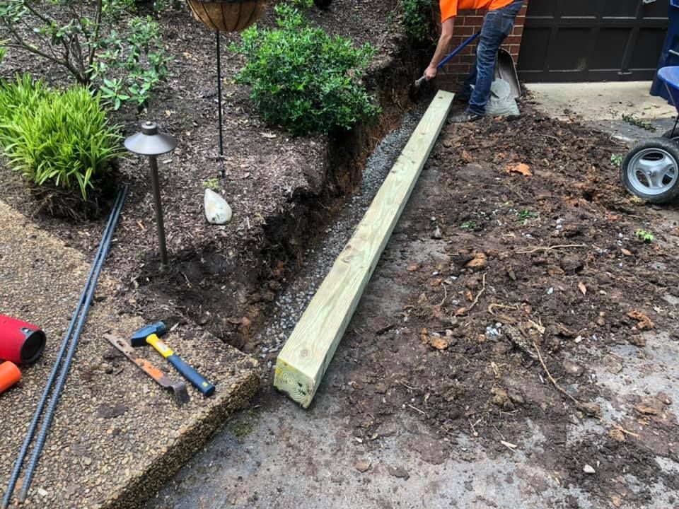 A man is digging a hole in the ground to install a wooden post.