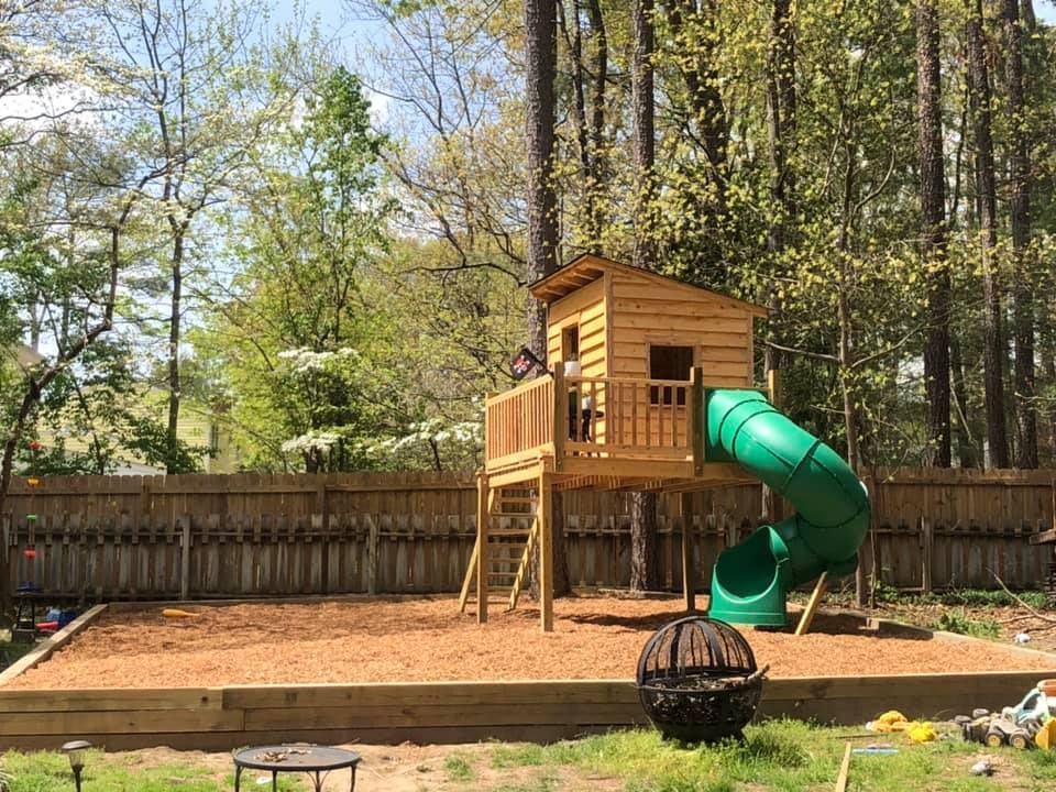 A wooden tree house with a green slide in a backyard.