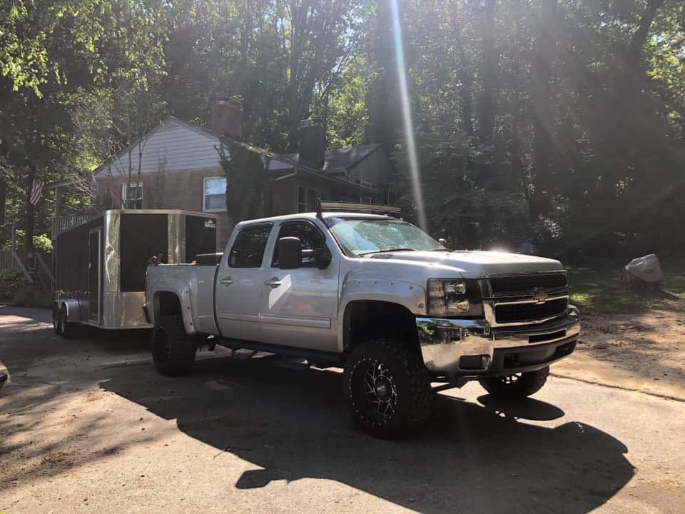 A silver truck is parked on the side of the road next to a trailer.