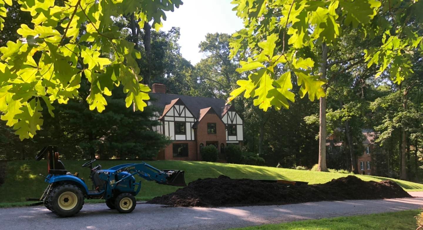 A blue tractor is parked in front of a large house