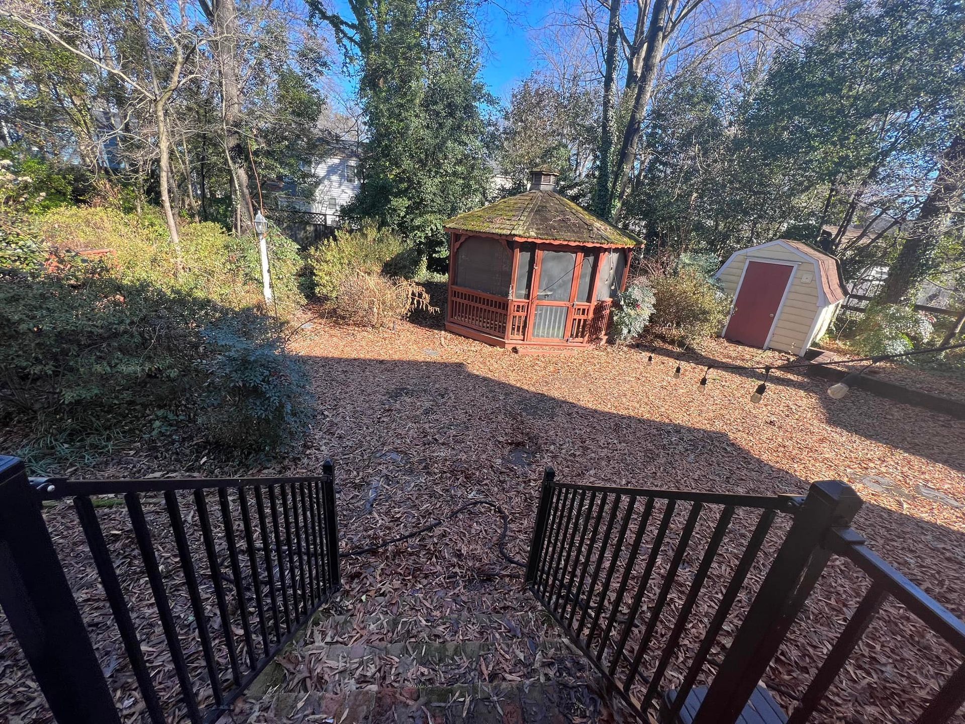 A gazebo is sitting in the middle of a yard surrounded by trees.