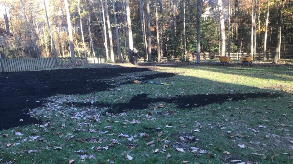 A large pile of black mulch is sitting on top of a lush green field.