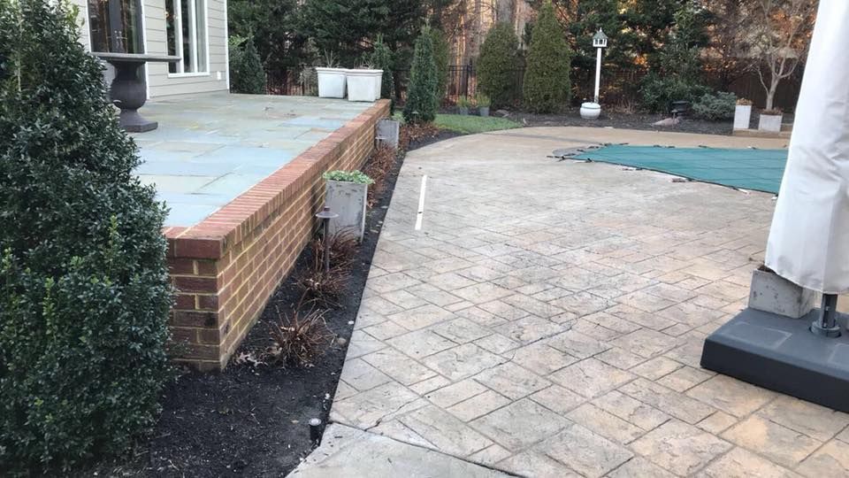 A patio with a brick wall , umbrella and a pool.
