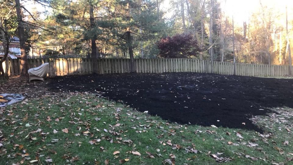 A backyard with a wooden fence and a large pond in the middle of it.