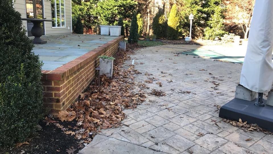 A patio with leaves on the ground and a brick wall.