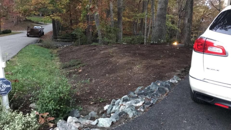 A white car is parked in a driveway next to a rock wall.