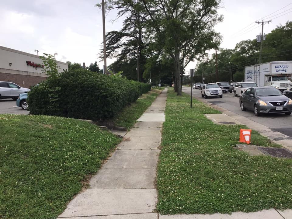 A row of cars are driving down a street next to a sidewalk