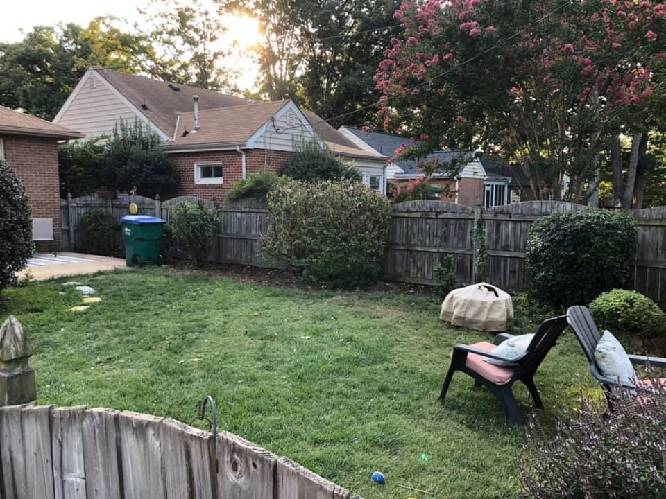 A backyard with a wooden fence , chairs , and a fire pit.