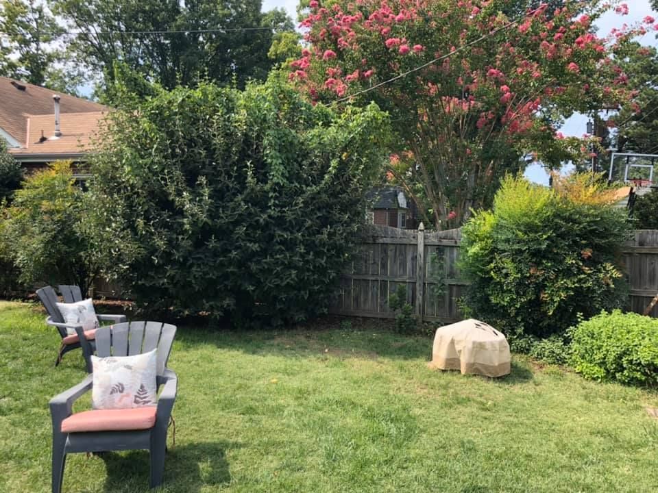 A backyard with lawn chairs , a fire pit and a fence.