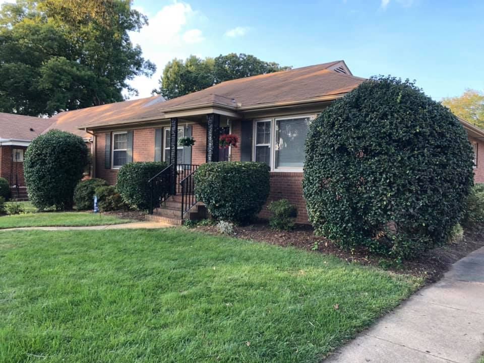 A brick house with a lush green lawn and bushes in front of it