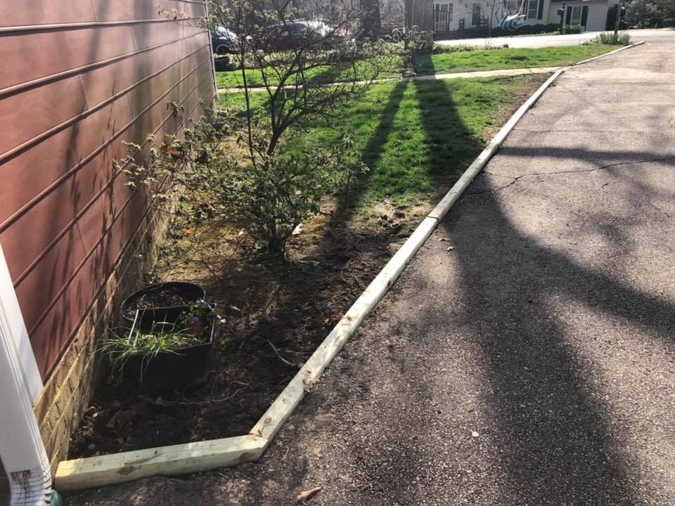 A wooden fence surrounds a corner of a yard next to a house.