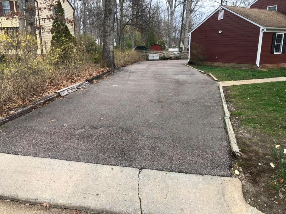 A driveway leading to a house with a red house in the background.