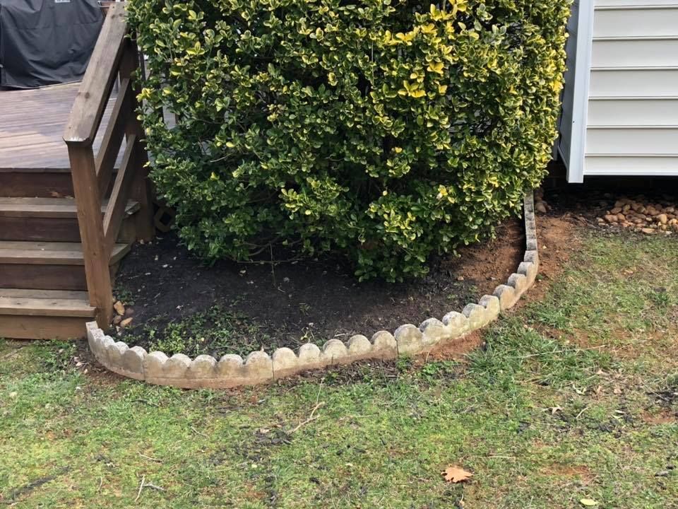 A concrete border around a bush in a yard next to a house.