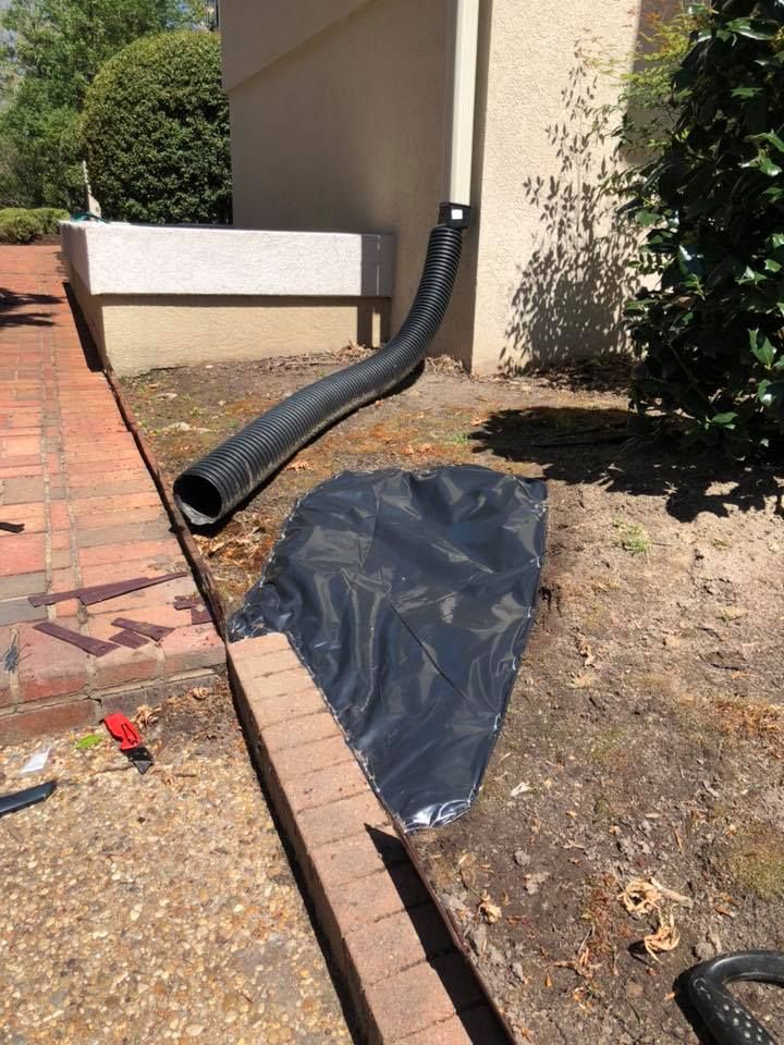 A black pipe is laying on the ground next to a brick sidewalk.