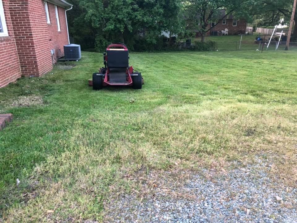 A lawn mower is sitting in the grass in front of a brick house.