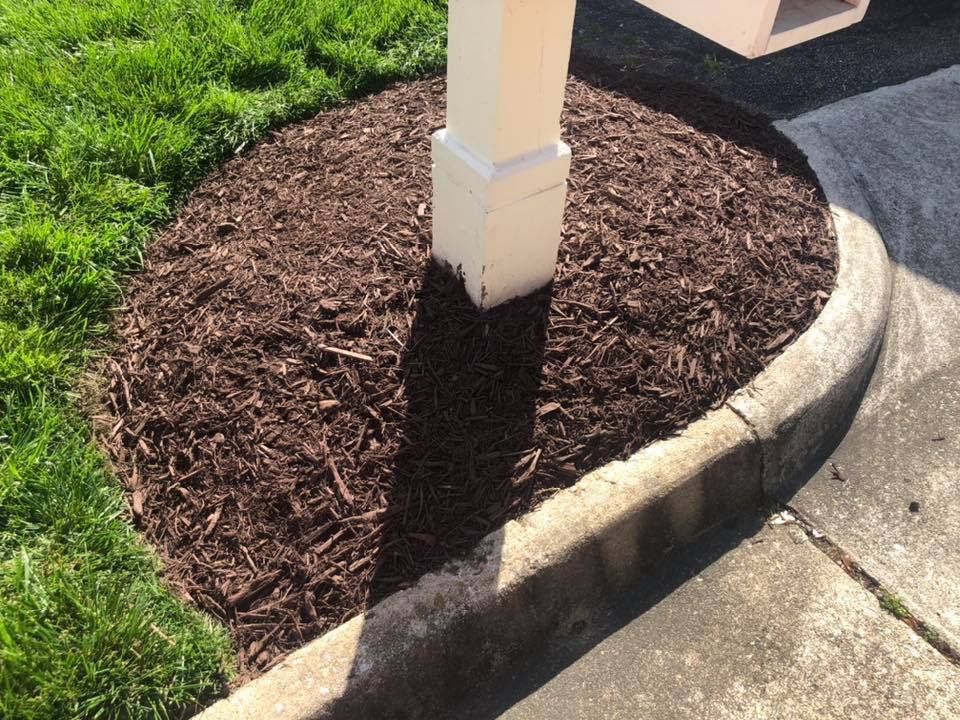 A white pole is sitting next to a pile of brown mulch.