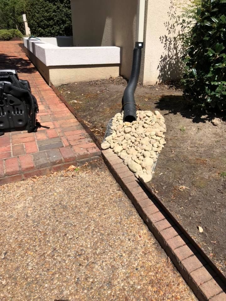 A drainpipe is sitting on top of a pile of rocks next to a brick walkway.