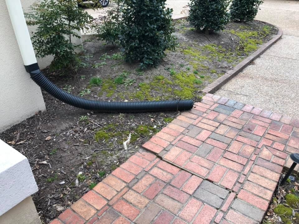 A drainpipe is attached to a brick walkway next to a house.
