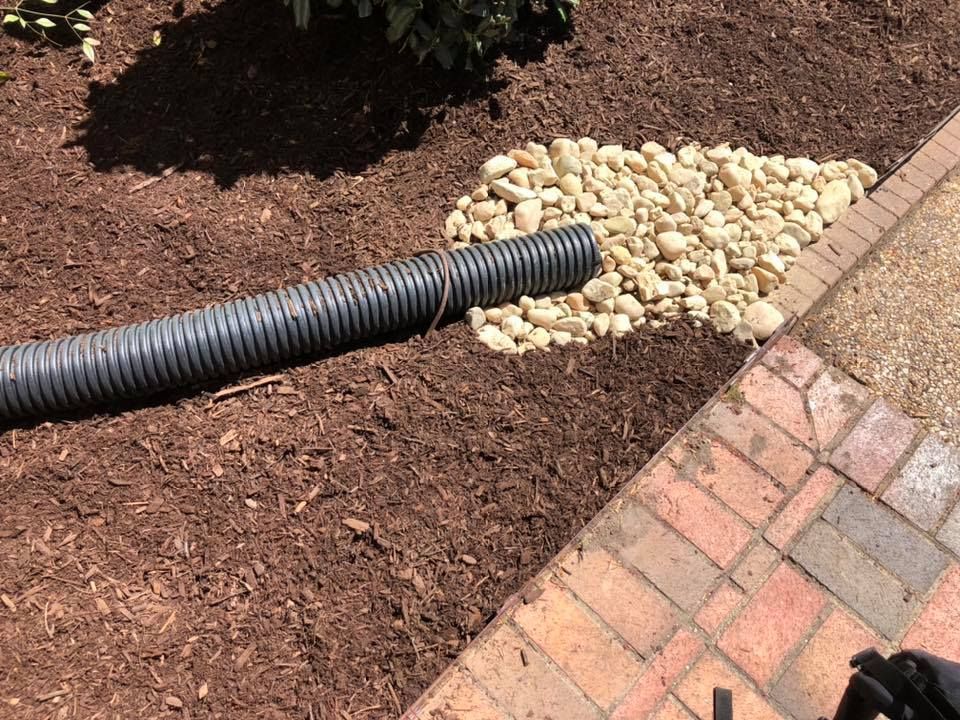 A drain pipe is sitting on top of a pile of rocks next to a brick walkway.