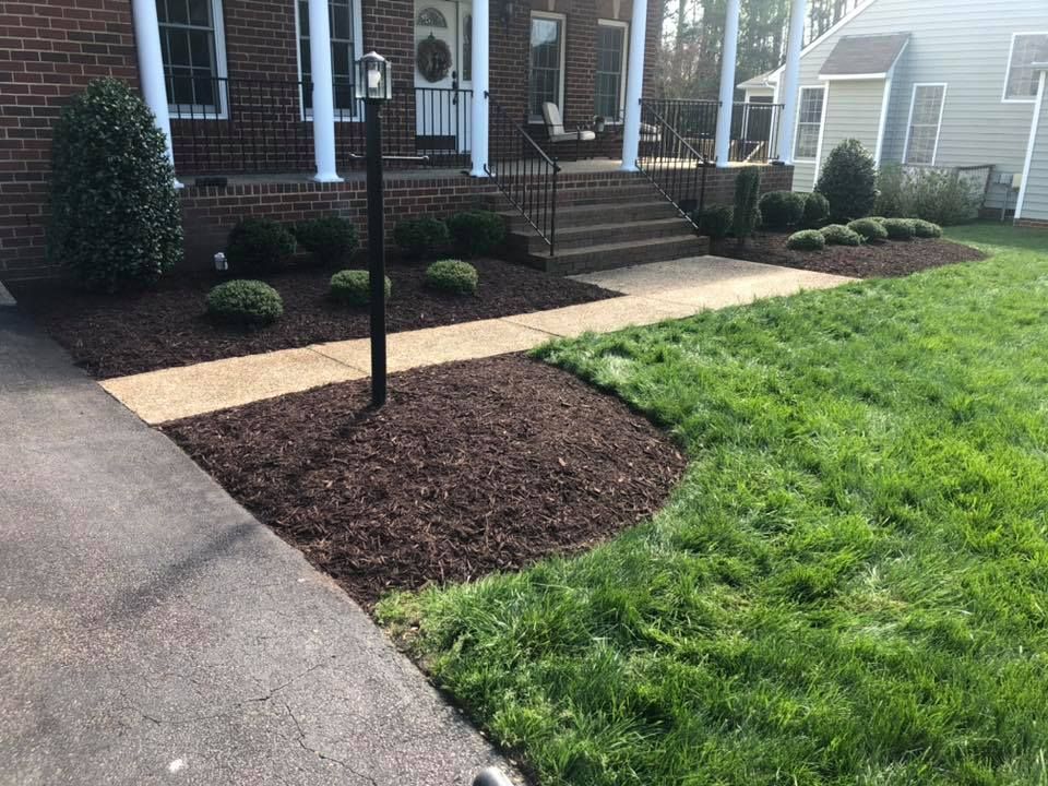 A brick house with a lush green lawn and a sidewalk in front of it.
