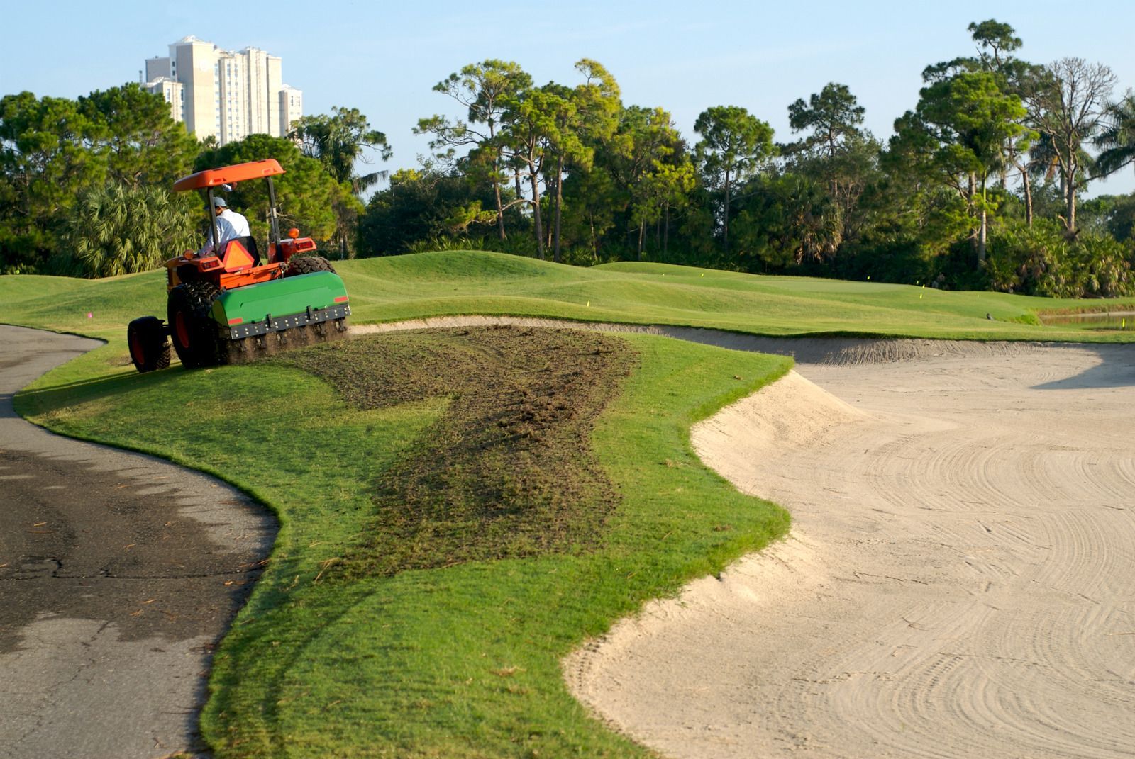 A man is driving a tractor on a golf course.