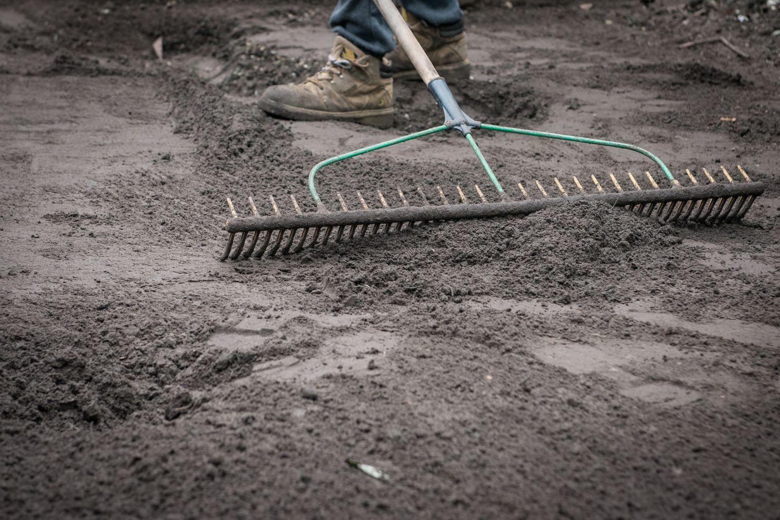 A person is raking dirt on the ground with a rake.