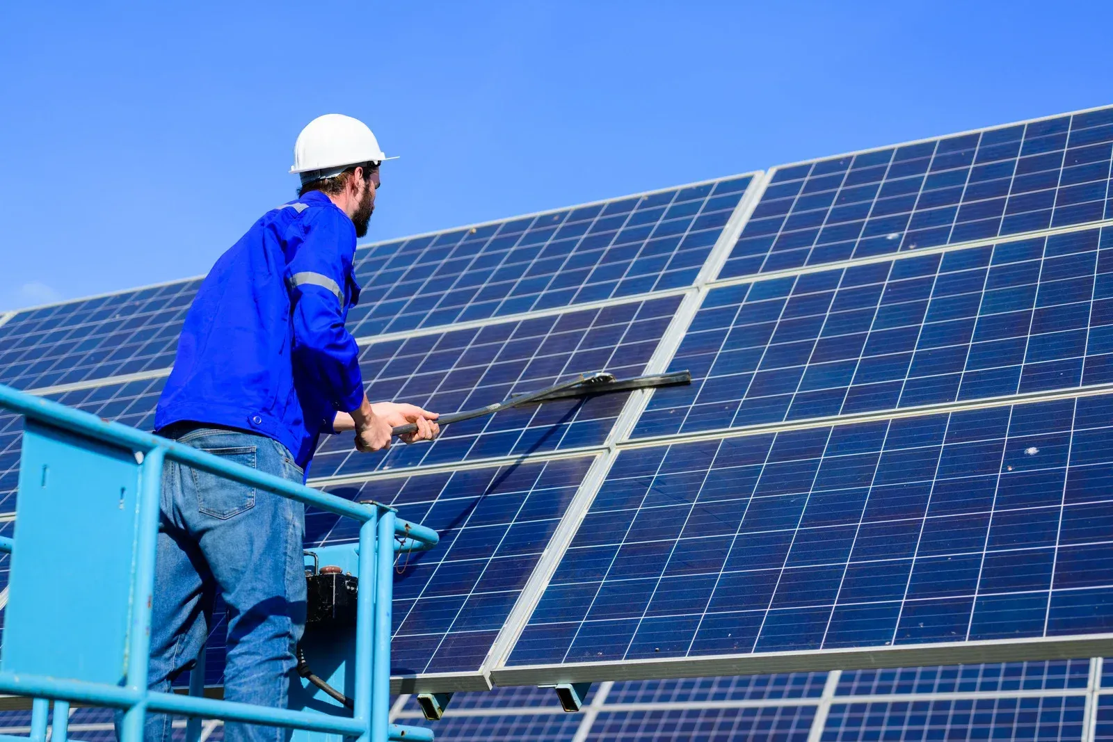 A man is cleaning solar panels on the roof of a building.