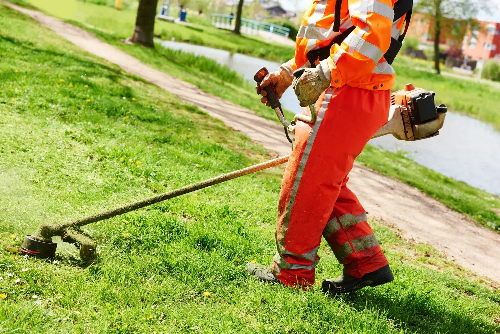 A man is cutting grass with a lawn mower in a park.