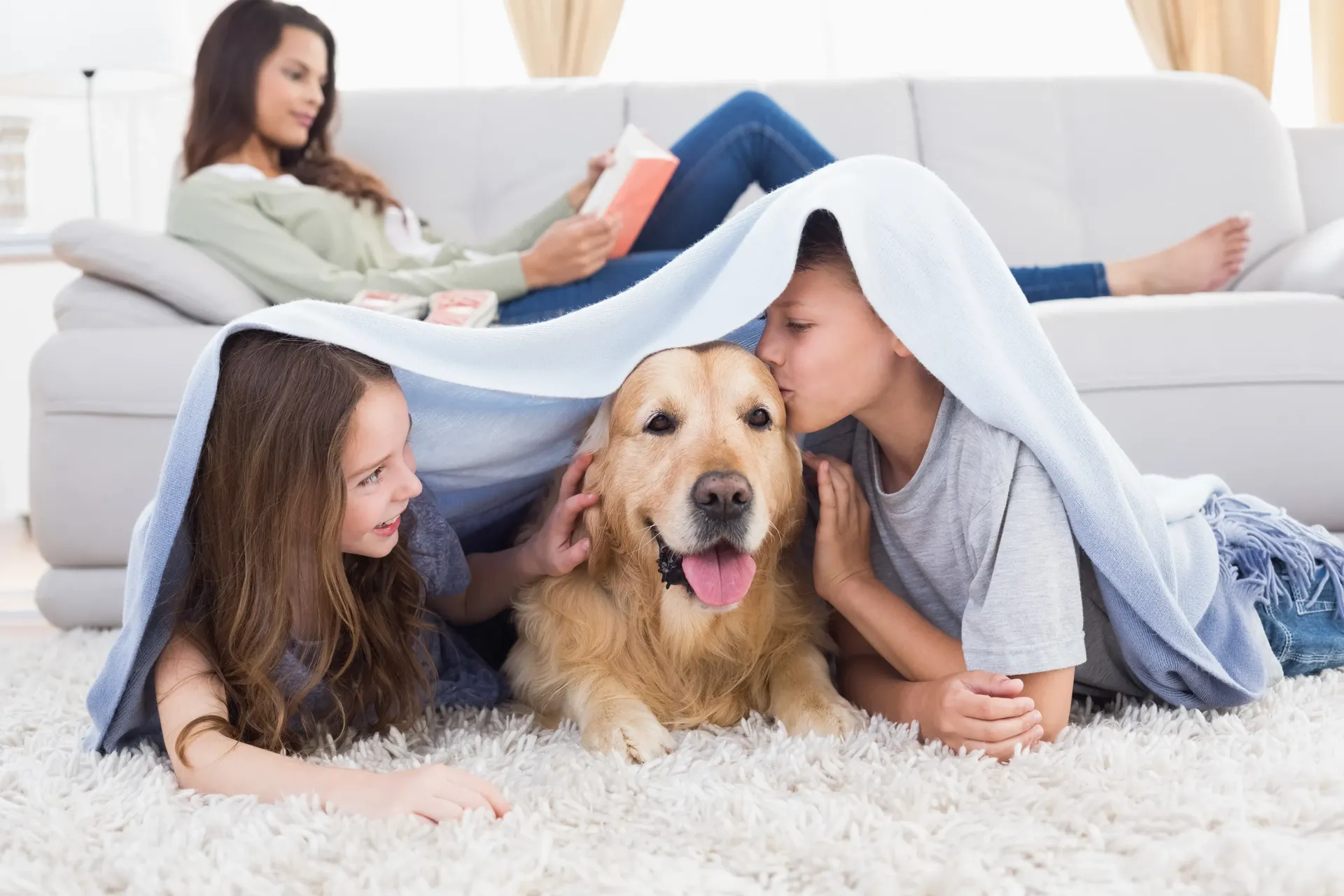 Children and dog lying on floor with a woman on a sofa in the background