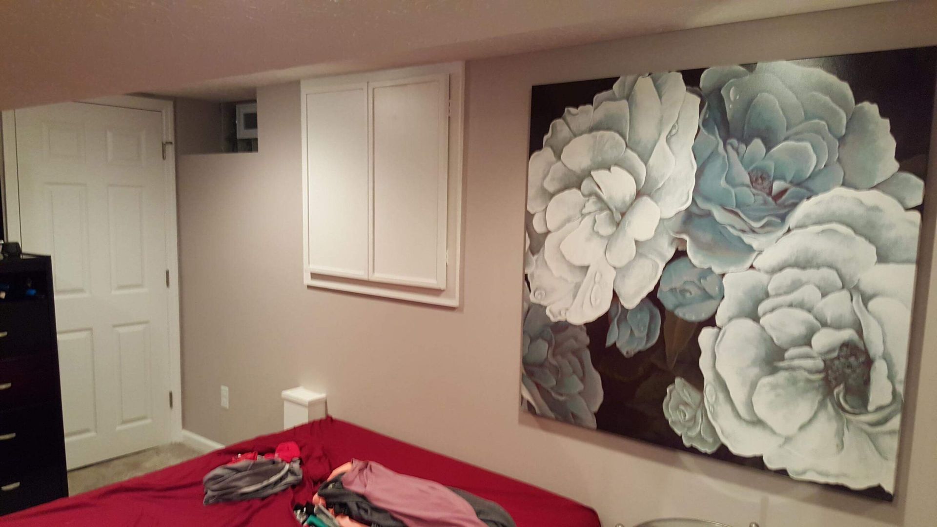 Bedroom with large floral painting, white cabinets, and red bedding.
