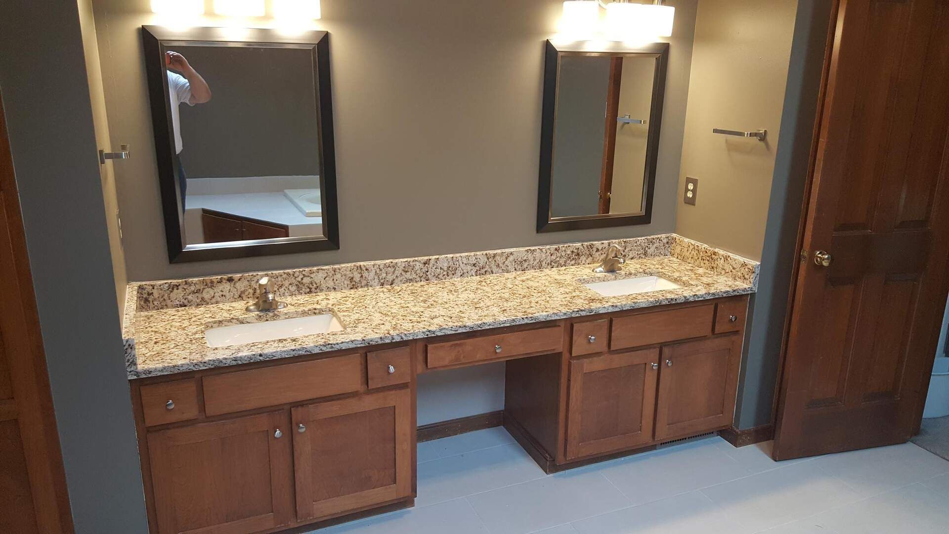 Bathroom vanity with two sinks, brown cabinets, granite countertop, mirrors, and lights.
