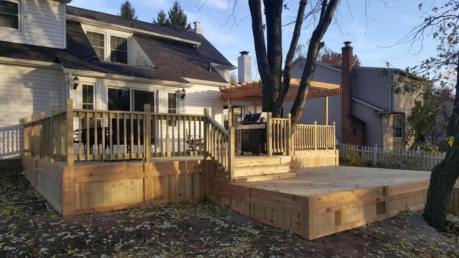 Wooden deck attached to a house, with stairs, railings, and a pergola.