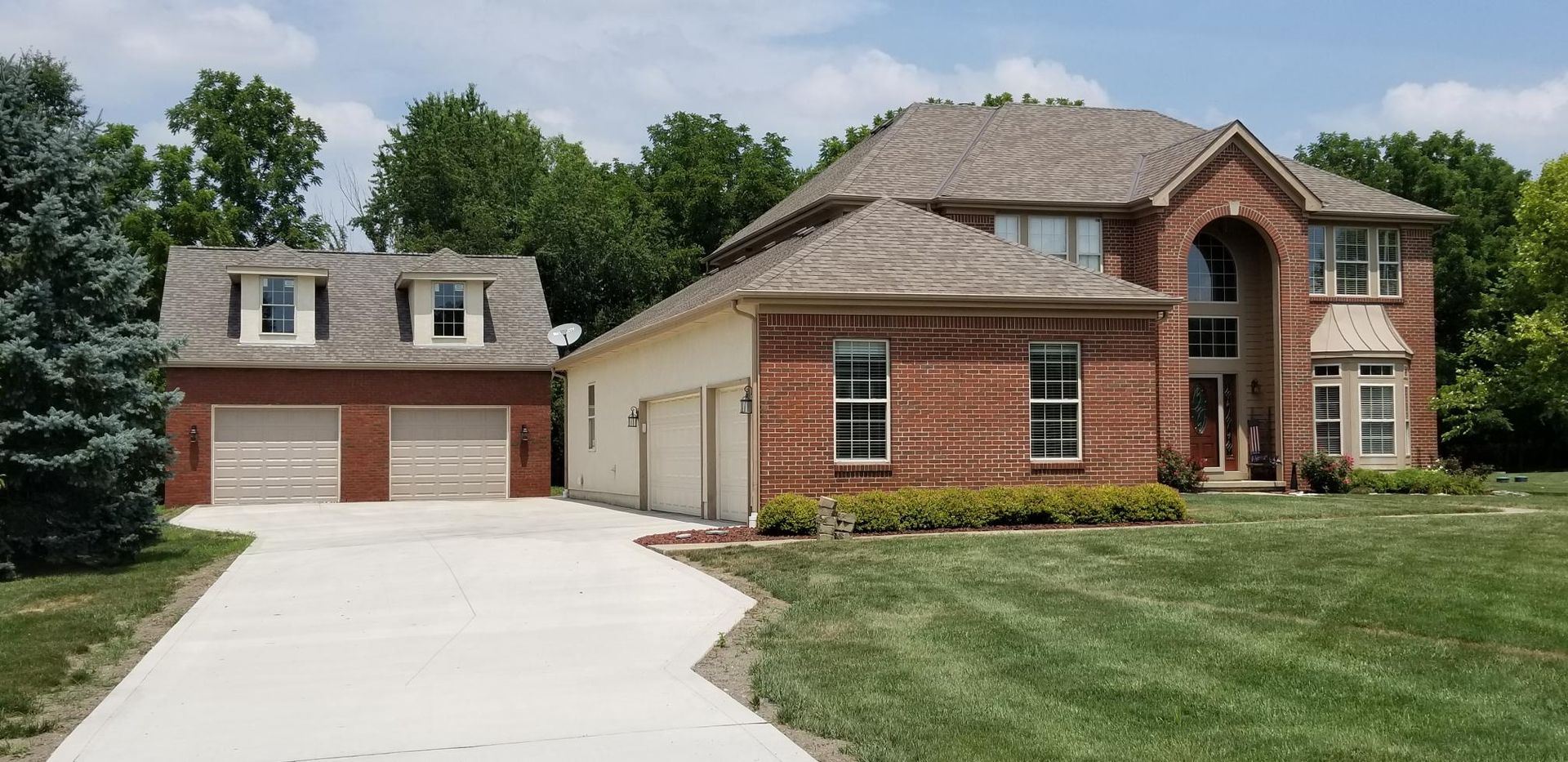 Brick home with driveway, garages, and well-manicured lawn, trees, and blue sky.