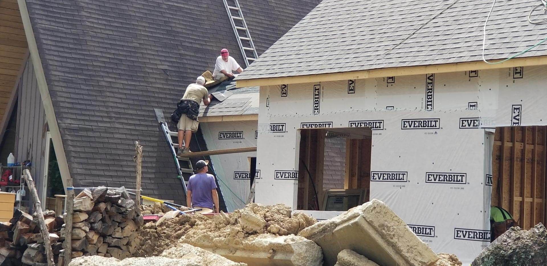 Roofers installing asphalt shingles on a residential roof; tools and materials visible.