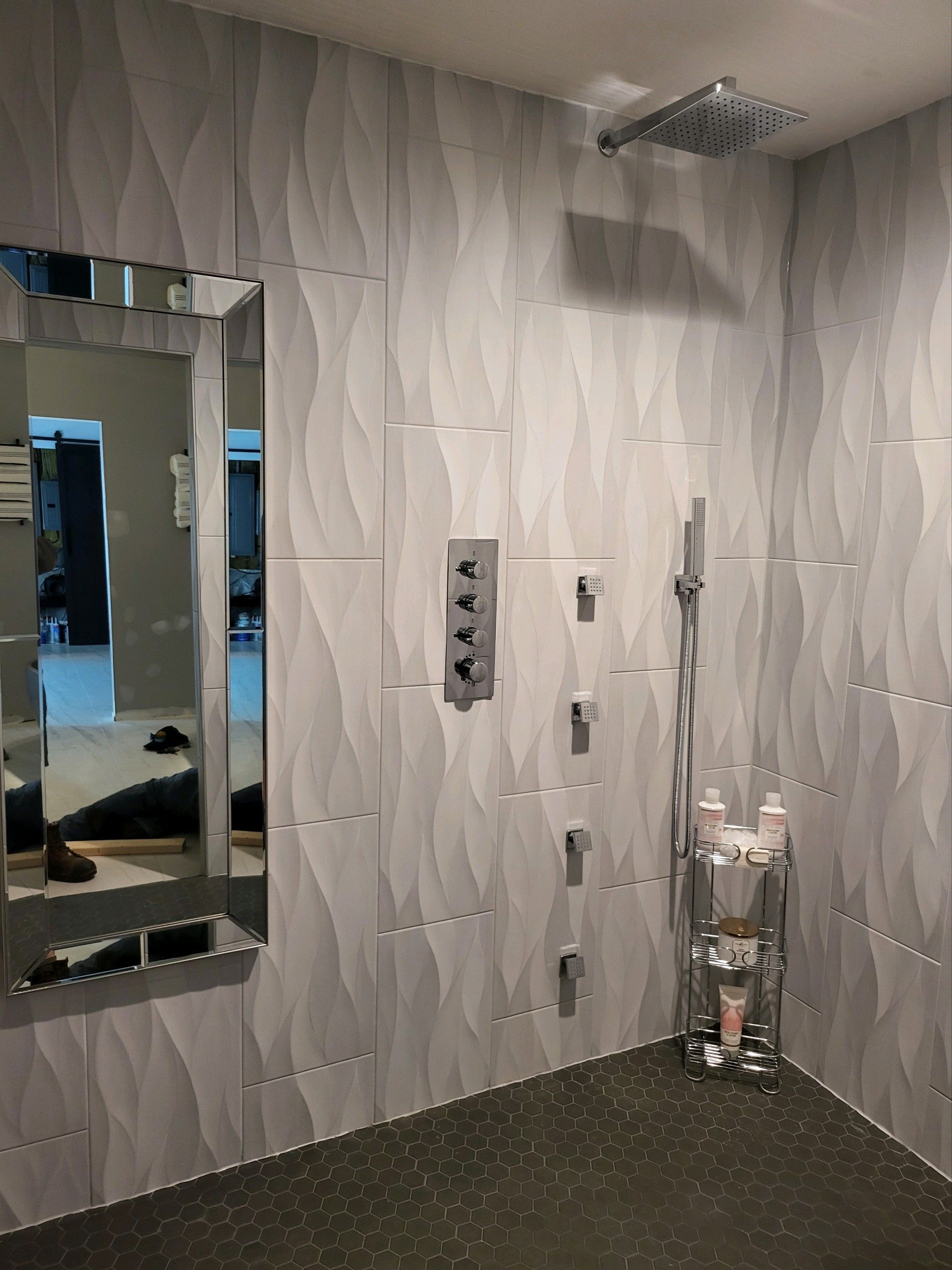Modern bathroom with gray wave-patterned tiles, showerhead, controls, handheld shower, and a mirror.